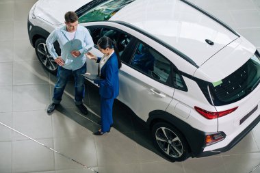 Dealership manager explaining payment details to customer when standing at automobile, view from above