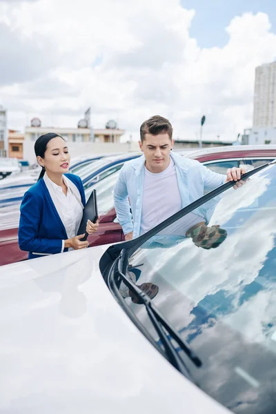 Carrancudo Jovem Olhando Para Automóveis Concessionária Carro Com Ajuda Gerente — Fotografia de Stock