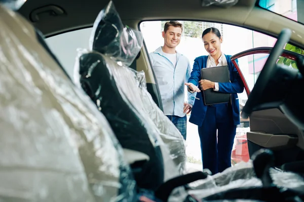 Sorridente Giovane Manager Concessionaria Che Mostra Interni Auto Avvolti Plastica — Foto Stock