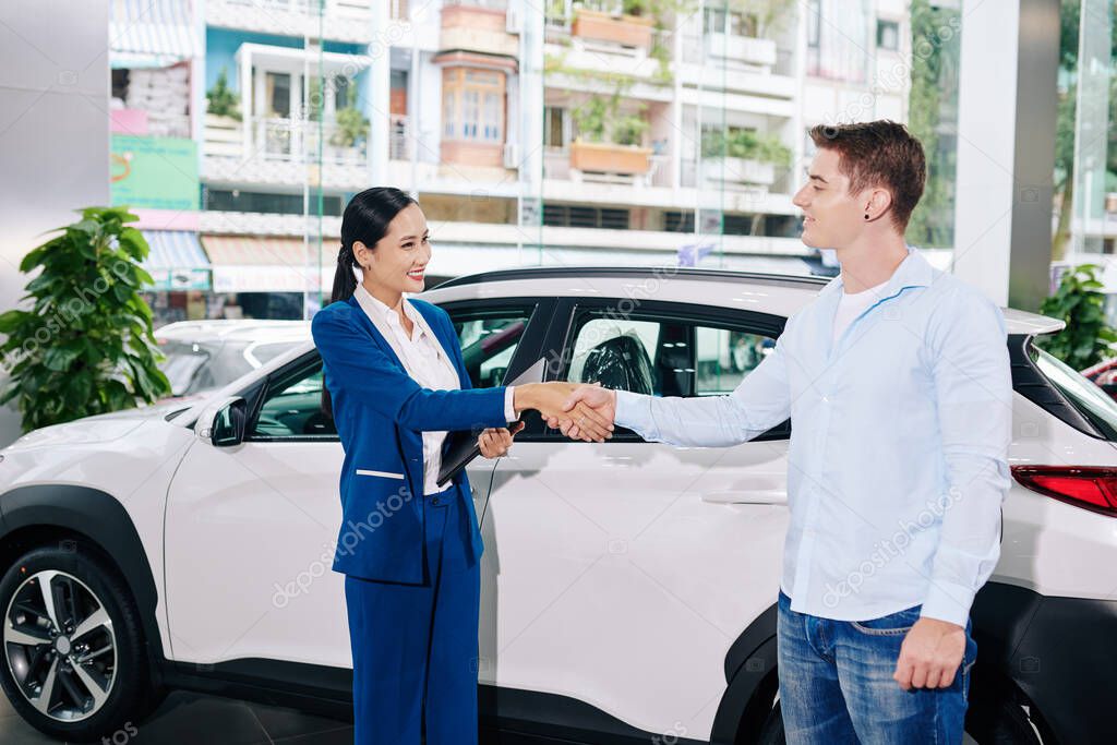 Smiling customer shaking hand of car dealership manager after buying automobile