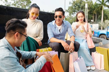 Pozitif Vietnamlı genç insanlar alışveriş merkezinden alışveriş yaptıktan sonra dışarıda oturup alışverişleri tartışıyor.