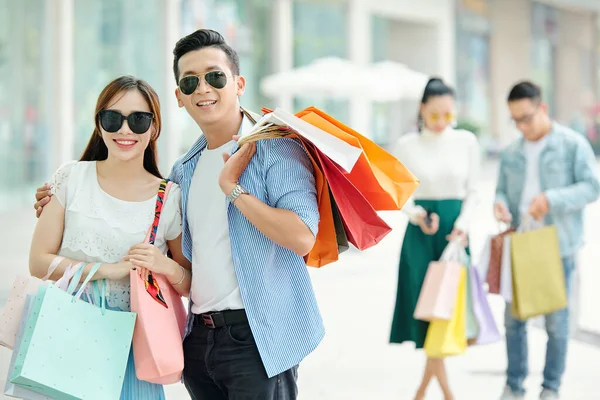 戴着太阳镜站在户外提购物袋的一对快乐的年轻夫妇 — 图库照片