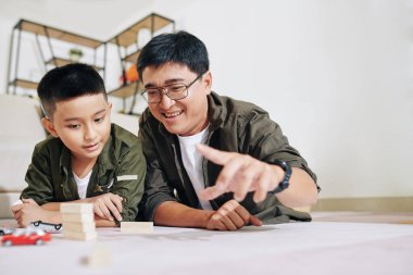 Oyuncak arabalarla ve tahta bloklarla oynayan neşeli orta yaşlı bir adam oyun odasında yerde yatarken