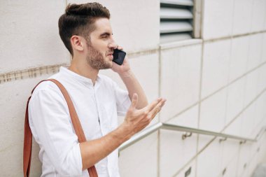 Duygusal genç sakallı adam telefonda iş arkadaşı ya da arkadaşıyla konuşurken hareketli hareketler yapıyor.