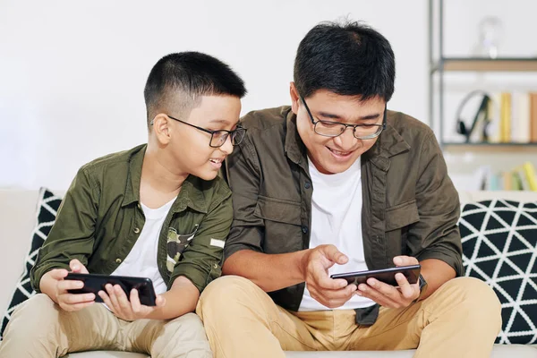 笑顔アジアの10代の少年は彼の興奮した父親の勝利ゲームのスマートフォン画面を見て — ストック写真