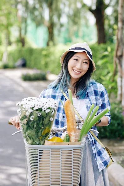 中国年轻女子骑自行车 提着花束和购物袋在篮子里笑的画像 — 图库照片