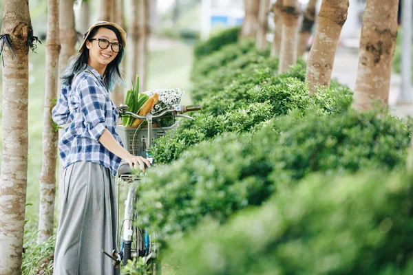 一个快乐的年轻中国女人 骑着自行车在公园里走着 回头对着相机笑着 — 图库照片