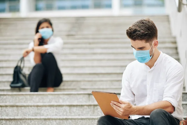 Serious Young Man Medical Mask Sitting Steps Reading Article Tablet — Stock Fotó