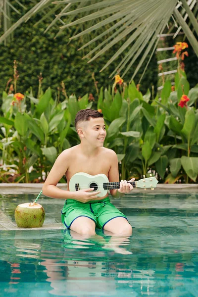 Glimlachende Gemengde Ras Tiener Jongen Zitten Het Zwembad Spelen Ukelele — Stockfoto