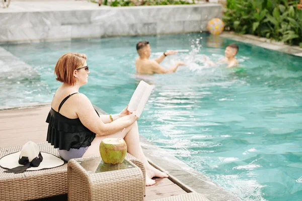 Mujer Sentada Chaise Lounge Leyendo Libro Cuando Marido Hijo Juegan — Foto de Stock