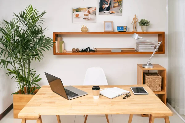 Opened laptop, digital tablet, planner and cup of coffee on table in modern office