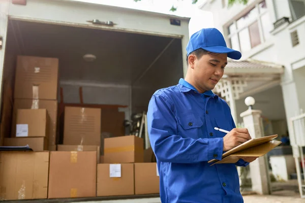 Vietnamese moving house company courier standing at delivery truck full of boxes and filling information in contract