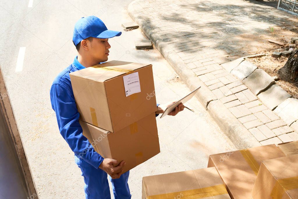 Young Asian delivery service worker checking data on digital tablet when unloading truck