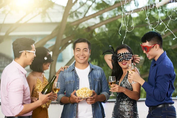 戴面具的快乐朋友们为拿着一碗爆米花的英俊年轻人举行了意想不到的生日宴会 — 图库照片