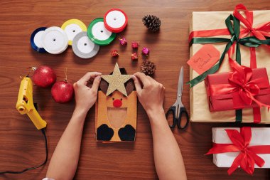 Noel hediyesi olarak geyik çantası hazırlayan yaratıcı kişinin elleri ve üzerine ışıldayan bir yıldız yapıştırmak.