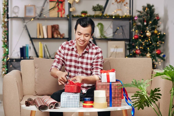 Cheerful Vietnamese Man Cutting Ribbon Wrapping Paper Wrapping Christmas Presents — 图库照片