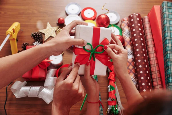 赤と緑の弓でクリスマスの贈り物を飾るカップルの手 — ストック写真
