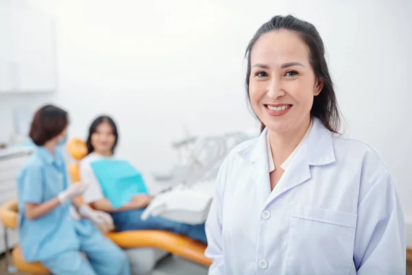 Vrolijke Ervaren Aziatische Orthodontist Glimlachen Camera Haar Assistent Praten Met — Stockfoto