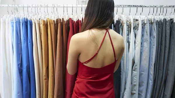 Młoda Kobieta Czerwonej Jedwabnej Sukience Wybiera Spodnie Stojaku Domu Towarowym — Zdjęcie stockowe