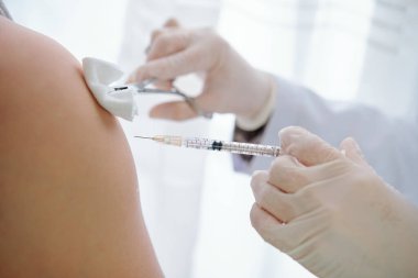 Coronavirus aşısı yapılmadan önce hastanın koluna pamuk yumağı enjekte eden hemşire elleri.