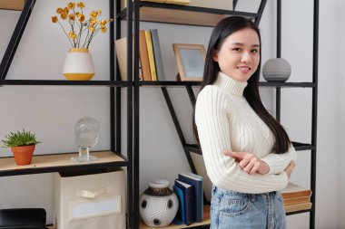 Dairede rafta duran ve kameraya gülümseyen kendine güvenen genç Asyalı kadının portresi.