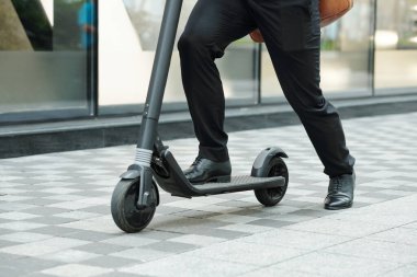 Sabahları aceleyle işe giderken elektrikli scooter kullanan bir adamın yakın plan görüntüsü.