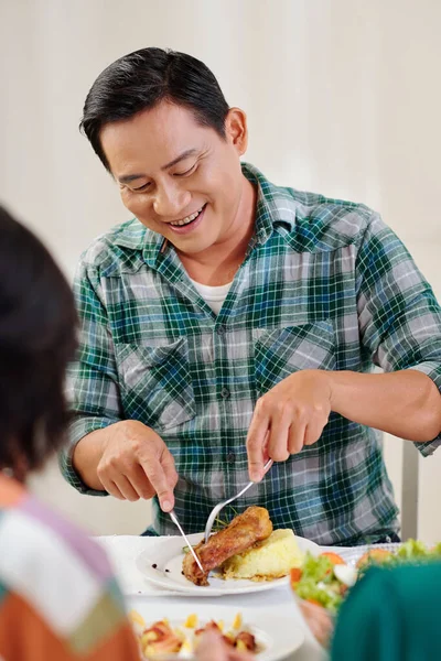 Happy mature Vietnamese man eating fried chicken and golden rice at dinner party