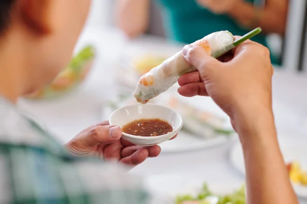 Close-up image of dinner party guest dipping spring roll in small bowl of sauce