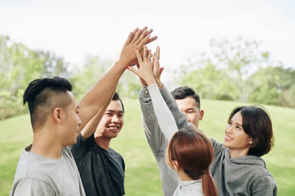 Cheerful young Asian people giving each other high five after finishing training outdoors