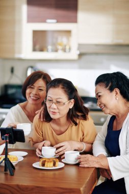 Gülümseyen yaşlı Asyalı kadınlar pastalarla çay içip kanalları için video kaydediyorlar.