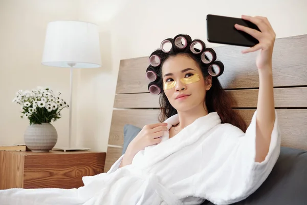 可愛いです若いですアジアの女性とともに毛ローラーオン頭の上に休憩後にベッドでお風呂と取り自画撮り — ストック写真
