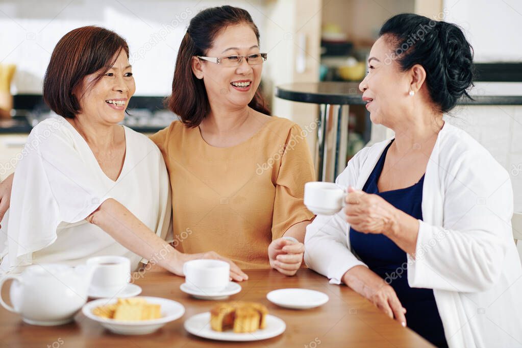 Group of cheerful Vietnamese senior women drinking tea with cookies and discussing news and gossips