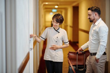 Genç, güzel, üniformalı otel müdürü misafirlere odanın kapısını elektronik anahtarla nasıl açacağını anlatıyor.