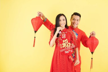 Kağıt fenerlerle poz veren mutlu genç Asyalı çift ve yeni yıl yazıtlarıyla duvar süslemeleri.