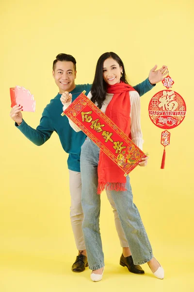 陽気若いですベトナムのカップルでスカーフや冬のセーターポージングで壁の装飾でハッピー新年の碑文 — ストック写真