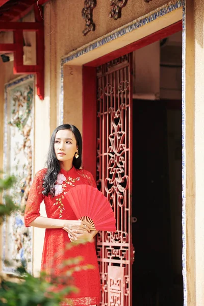 一个心事重重的年轻亚洲女人手拿着纸扇站在门口 — 图库照片