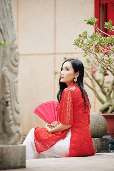 穿着越南传统服装的年轻貌美的女士手拿纸扇坐在户外 — 图库照片