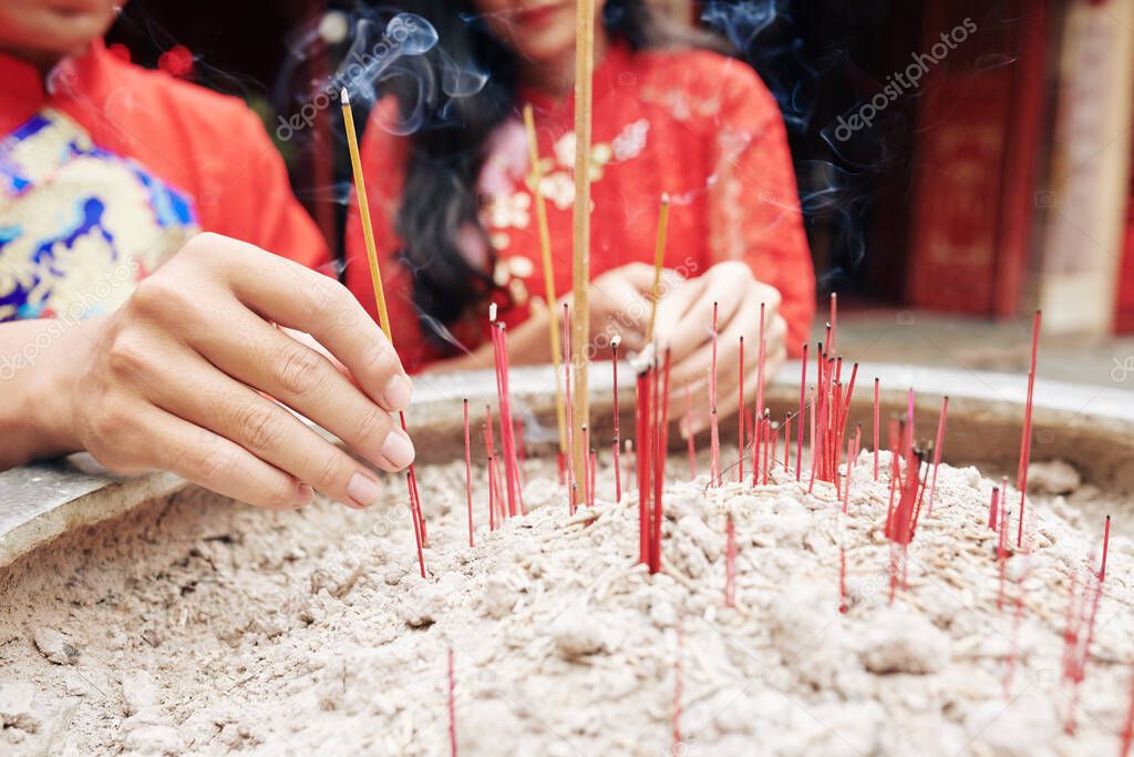 Close-up image of young people putting smoking sticks in copper urn in Buddhism temple on Lunar New Year