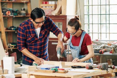 Tecrübeli bir marangoz, kadın çırağına tahta delmeyi öğretiyor.
