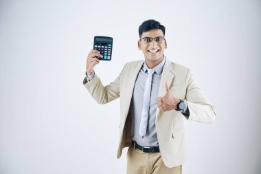 Elindeki hesap makinesiyle mutlu ve heyecanlı genç girişimci başparmaklarını kaldırıyor ve beyaz üzerine izole edilmiş kameraya bakıyor.