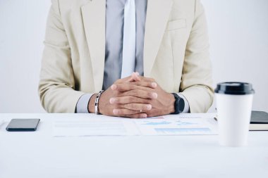 Ofis masasında elinde dosyalar, belgeler ve bir fincan kahve ile oturan kendine güvenen girişimcinin kırpılmış görüntüsü.