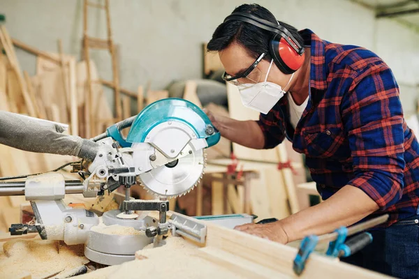 円形ののこぎりで木製の板を切断保護マスク イヤーマフやゴーグルのプロの大工 — ストック写真
