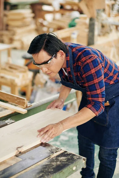 木製工場の工具で作業エプロンやゴーグルの深刻な大工と円形の刃で木板を切断 — ストック写真