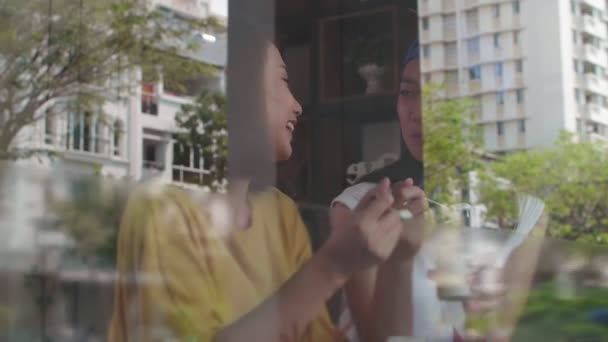 跟踪两个年轻的亚洲女人坐在窗后的咖啡厅里 吃着冰激凌 边说话 — 图库视频影像