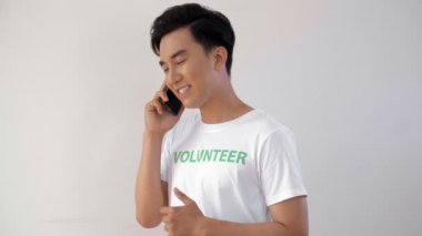 Asyalı genç bir adam elinde telefonla kameraya bakıp gülümsüyor.