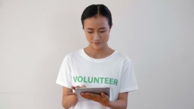 Kadın Asyalı gönüllü elinde tabletle duruyor, bilgileri tarıyor, sonra kameraya bakıyor ve gülümsüyor.