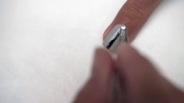 Kadın elinin cilalanmış kadın tırnağına parlak gümüş elmaslar sürerken yakın plan.