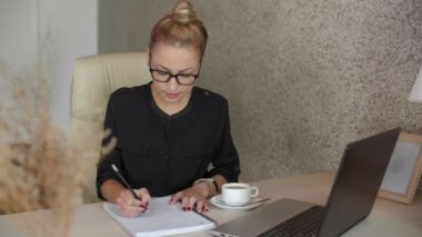 Kafkasyalı iş kadınının masaüstünde oturup kalemle defterine çizdiği ve sonra da bardakları burnunun köprüsüne ittiği orta boy bir fotoğraf.