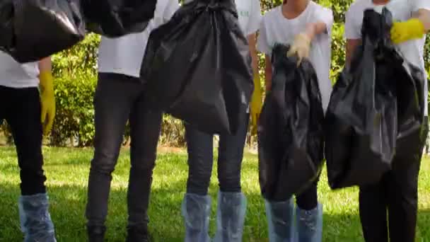 Yüzlerinde Gülümsemeyle Çimenlikten Siyah Çöp Torbalarını Alan Asyalı Genç Gönüllüleri — Stok video