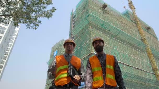建物の近くに立って親指を立てる安全ベストと硬い帽子を身に着けている2人の男性建築家の低角度ビュー — ストック動画
